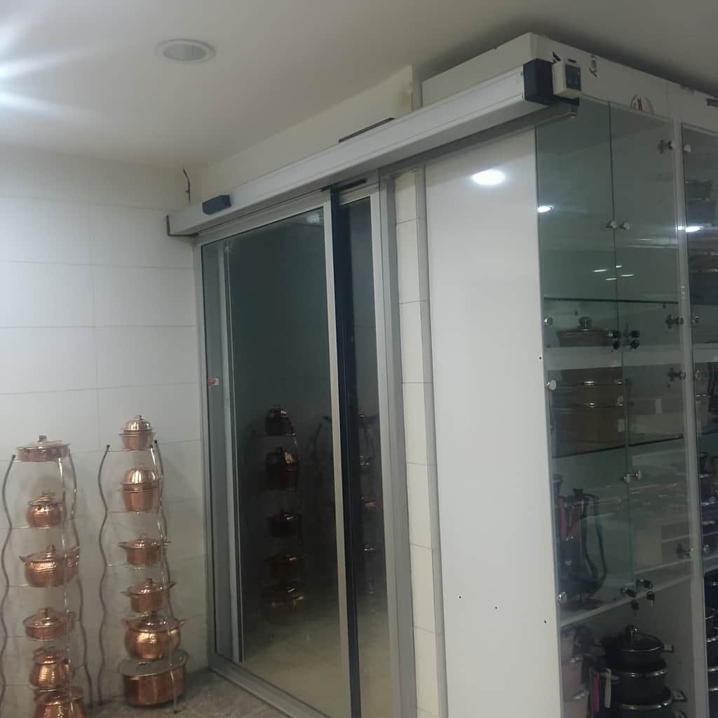 درب اتوماتیک شیشه ای لولایی سنسوردار فریم لس با نمای مدرن